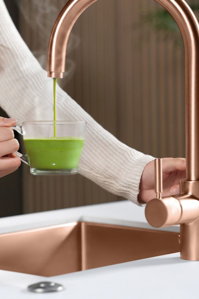 Rose gold tap dispensing instant matcha into a glass mug