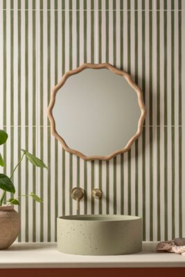 Green stripe tiled bathroom with a wavy bamboo-frame circular mirror and a pale green stone sink