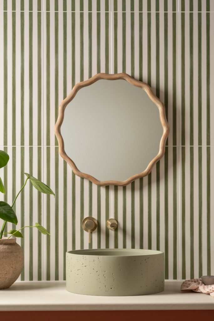 Green stripe tiled bathroom with a wavy bamboo-frame circular mirror and a pale green stone sink
