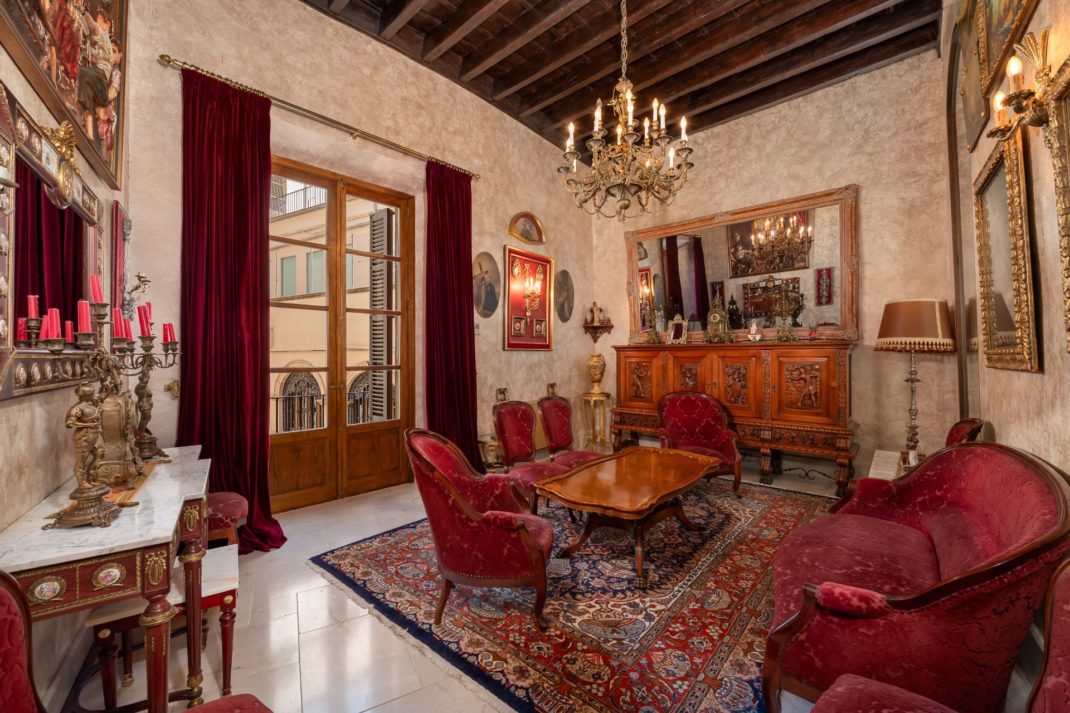 Palace living room with stone floors, wooden ceiling beams, chandelier and red velvet furniture