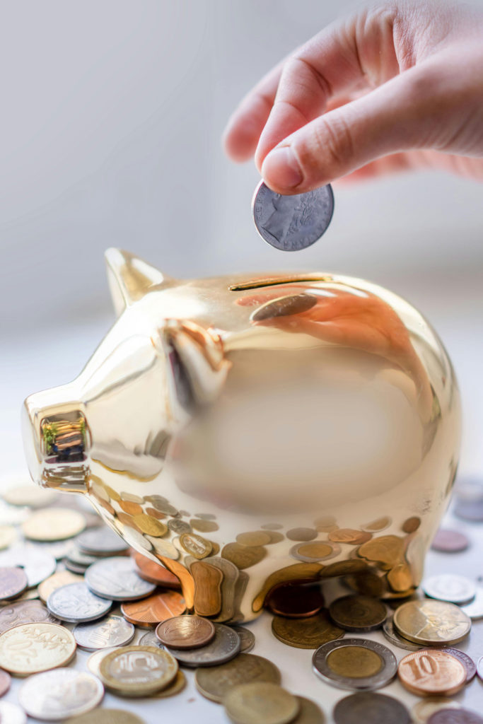 A hand putting a coin in a gold piggy bank