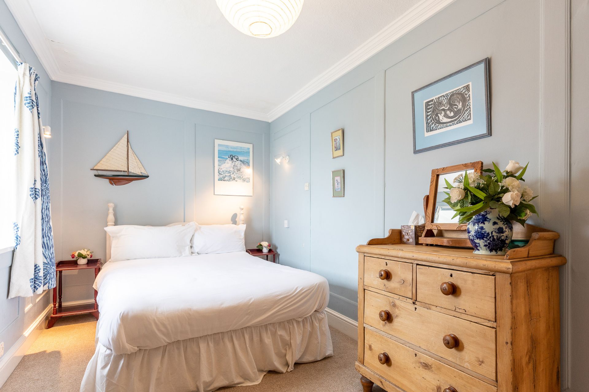 Bedroom with pale blue walls, white bedding and a wooden dresser