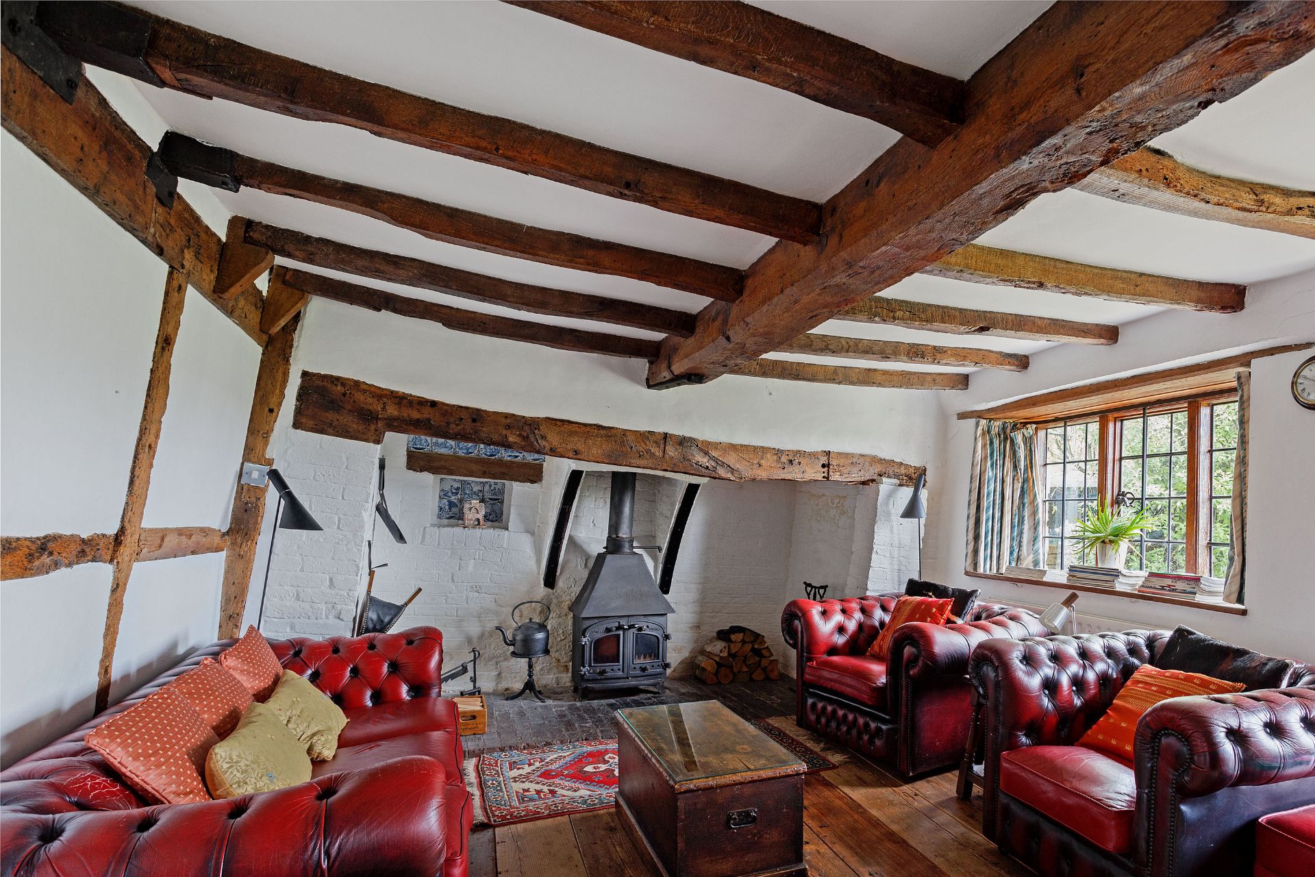 Living room with wooden beams, red leather sofas and a woodburning stove