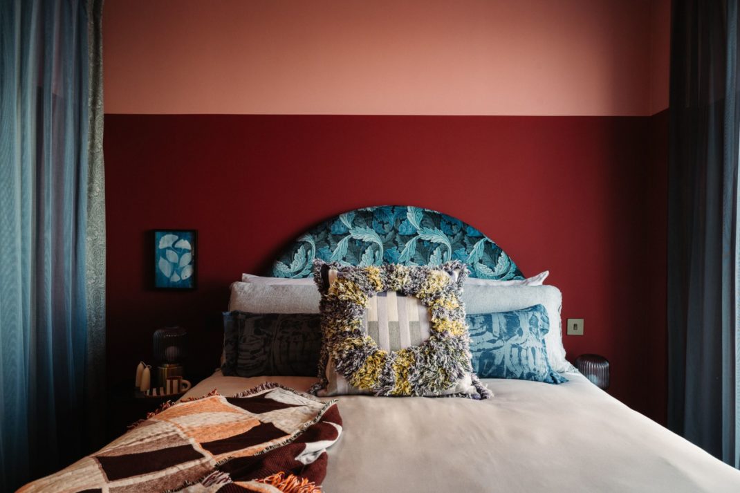 Bedroom with terracotta and red feature wall, patterned blue headboard and white bedding