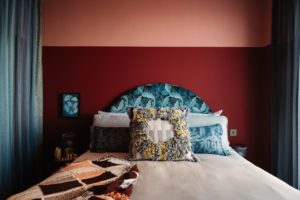 Bedroom with terracotta and red feature wall, patterned blue headboard and white bedding