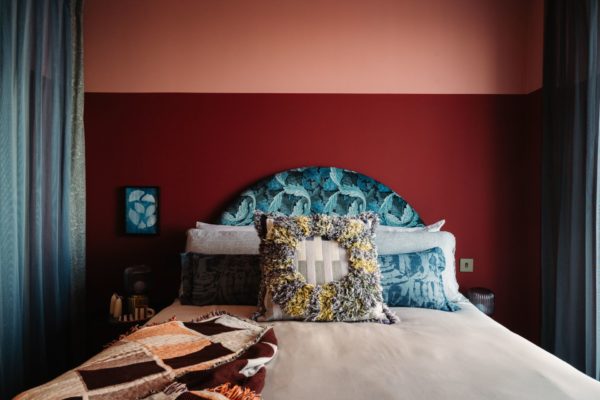 Bedroom with terracotta and red feature wall, patterned blue headboard and white bedding