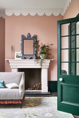 Pale pink living room with white scalloped cornicing, a white fireplace, a grey striped sofa and a dark green door