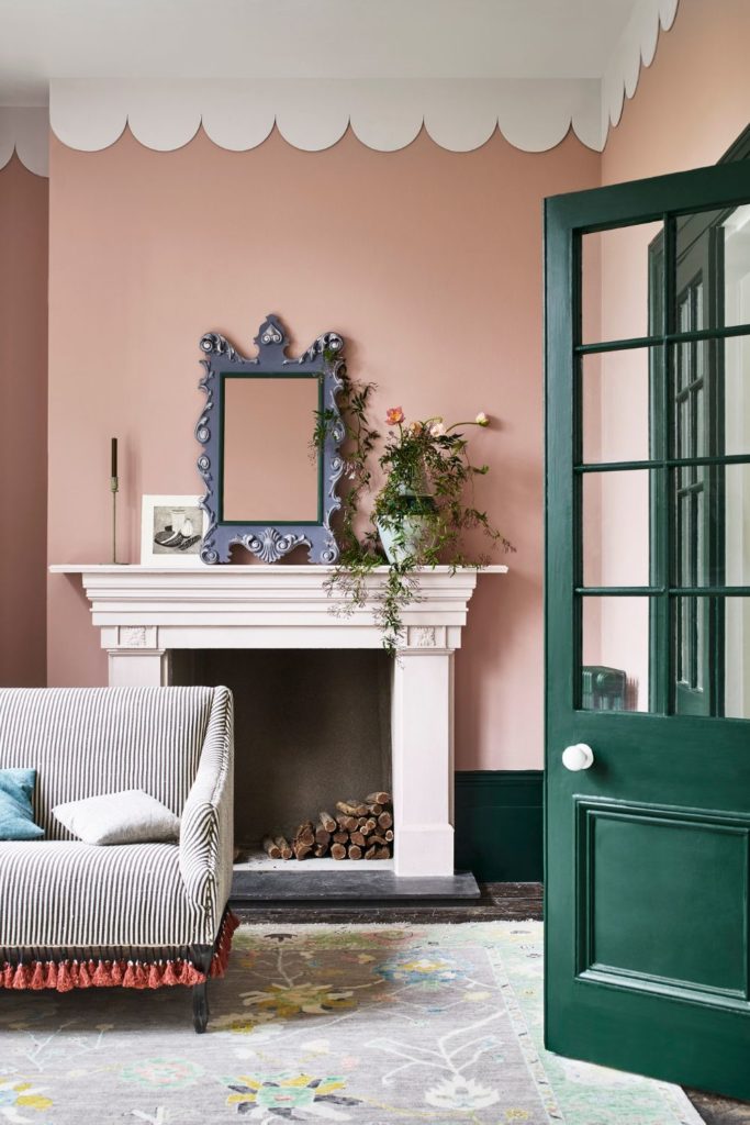 Pale pink living room with white scalloped cornicing, a white fireplace, a grey striped sofa and a dark green door