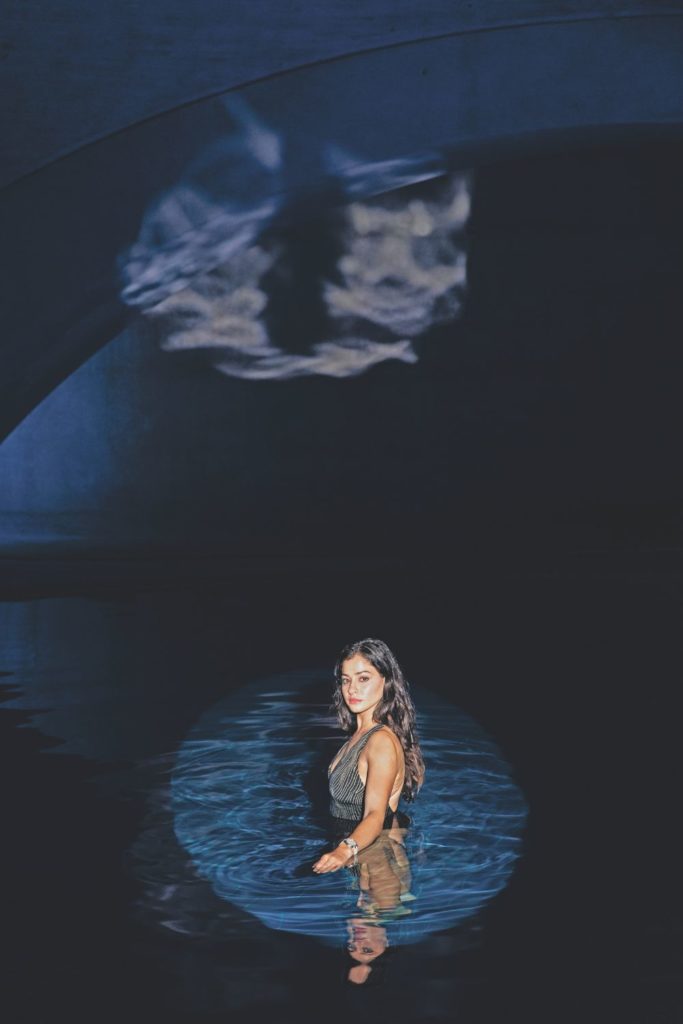 Swimmer Yusra Mardini standing in a dark pool with a spotlight on her
