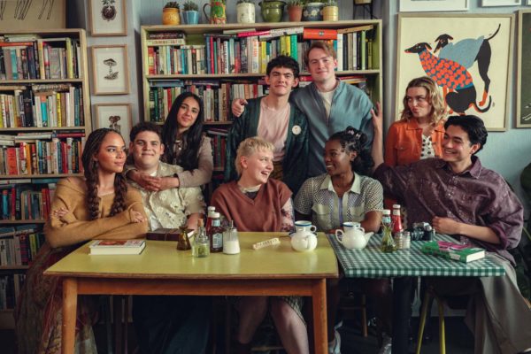 The core cast of Heartstopper Forever gathered around a table, smiling at the camera and each other