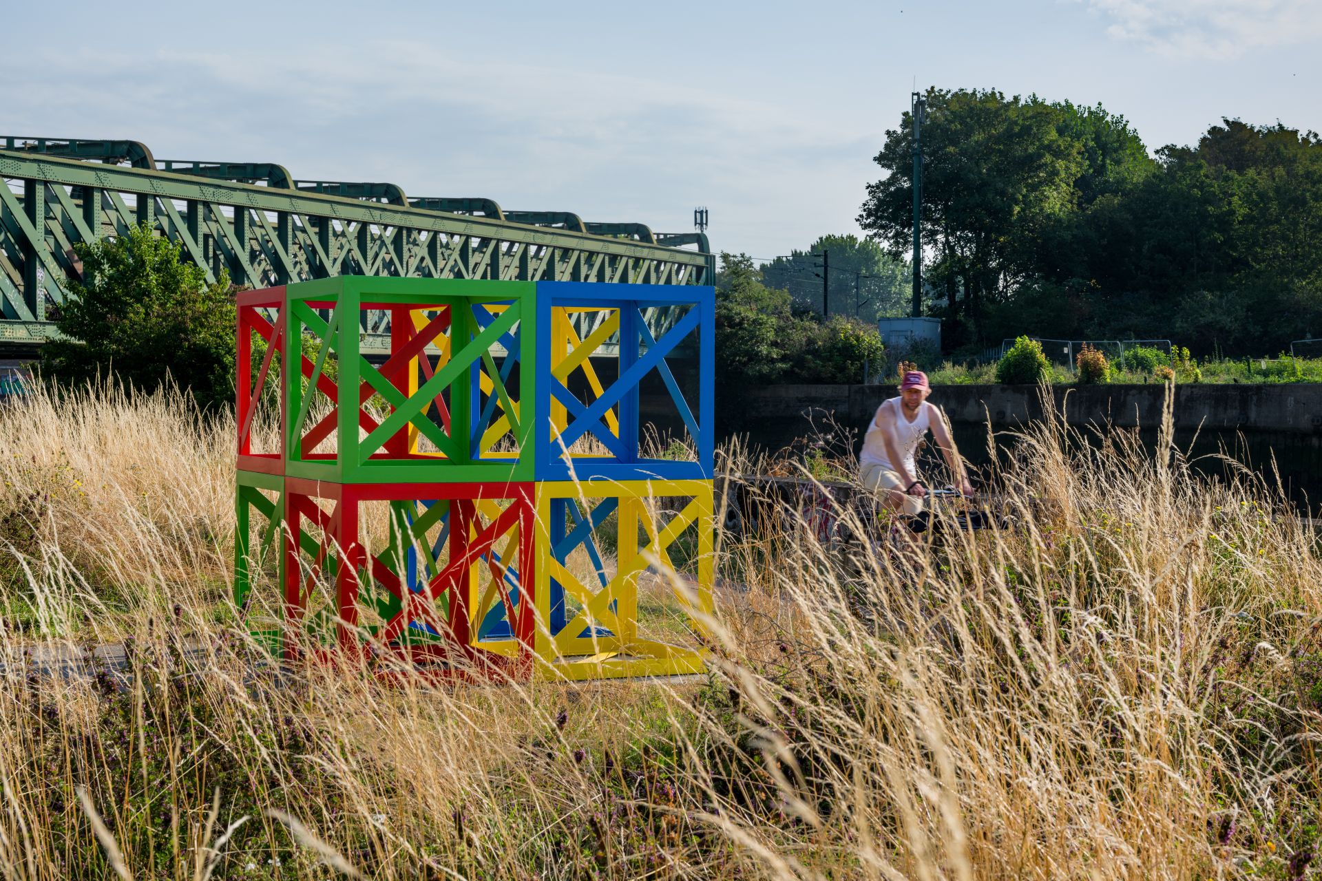 A cyclist going past a multicoloured art work surround by long grass
