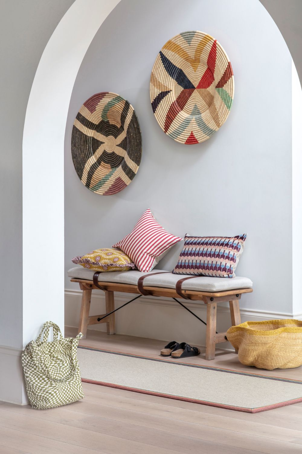 Hallway with white archway, beige runner, wooden bench with grey cushion, and colourful woven wall plates