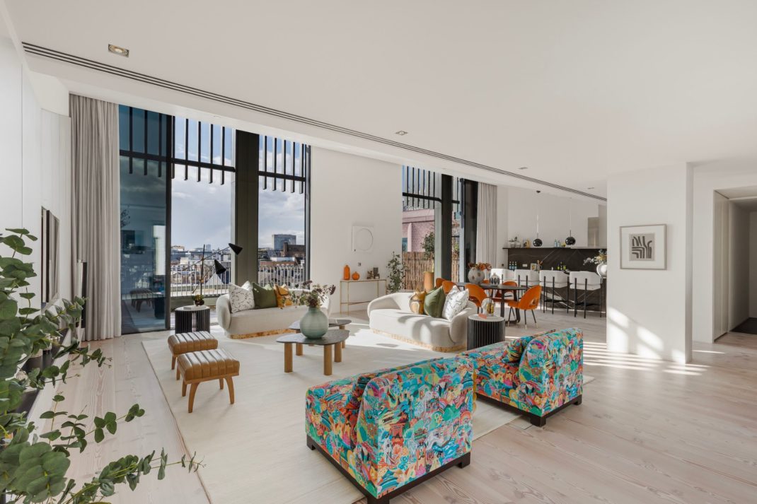 Penthouse living space with blue and yellow colour-splatter armchairs, boucle sofas and French doors