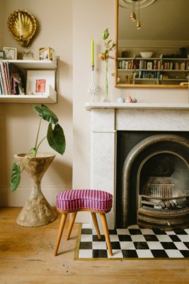 Living room with marble fireplace, pink and red striped stool, and checkerboard tiling
