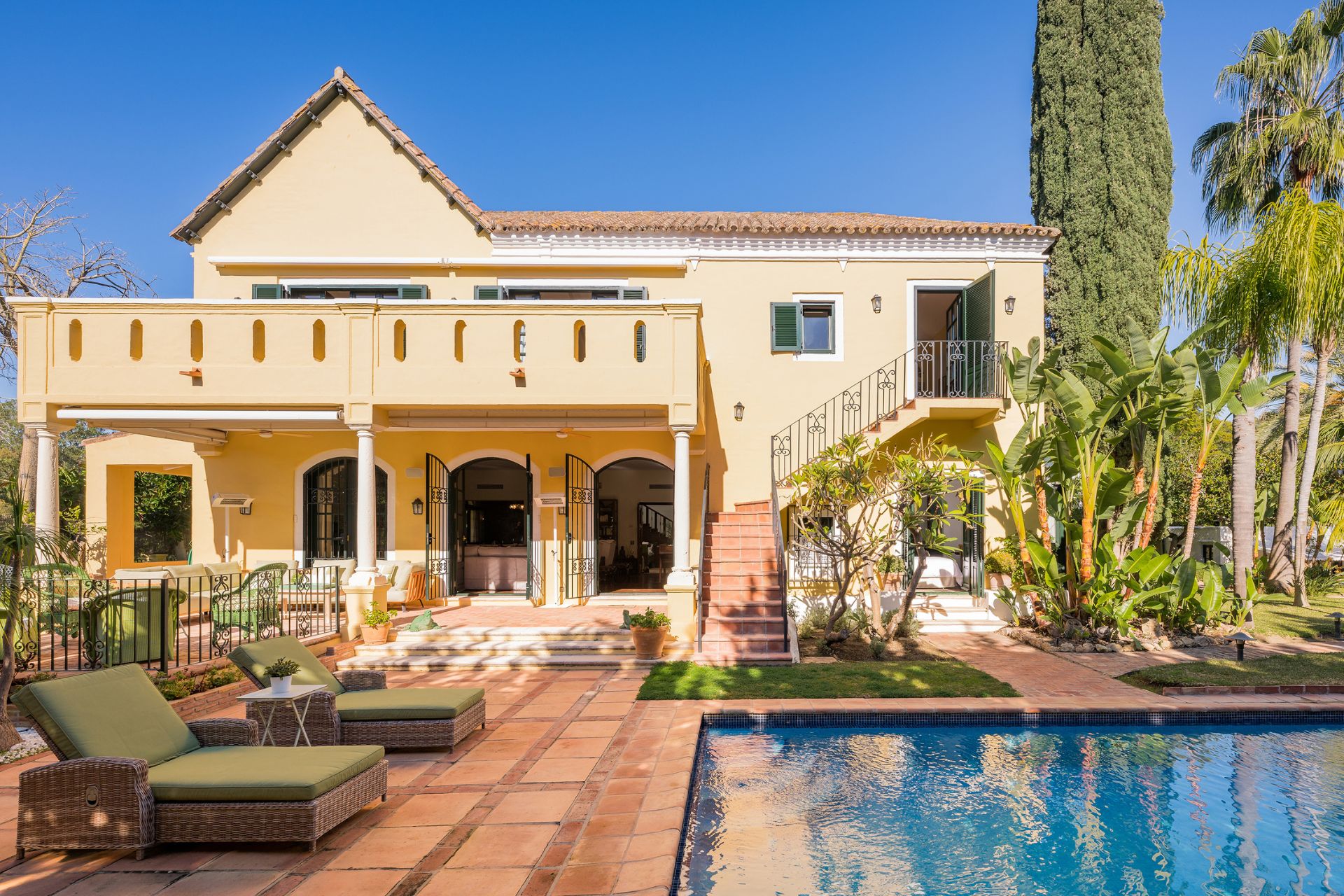 Villa with stone terrace, green garden furniture, and outdoor pool