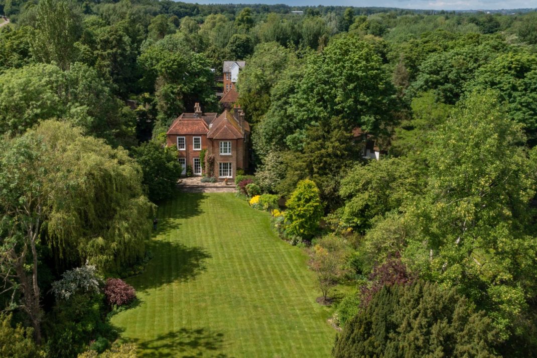 Aerial view of red brick country home surrounded by trees and a sweeping lawn