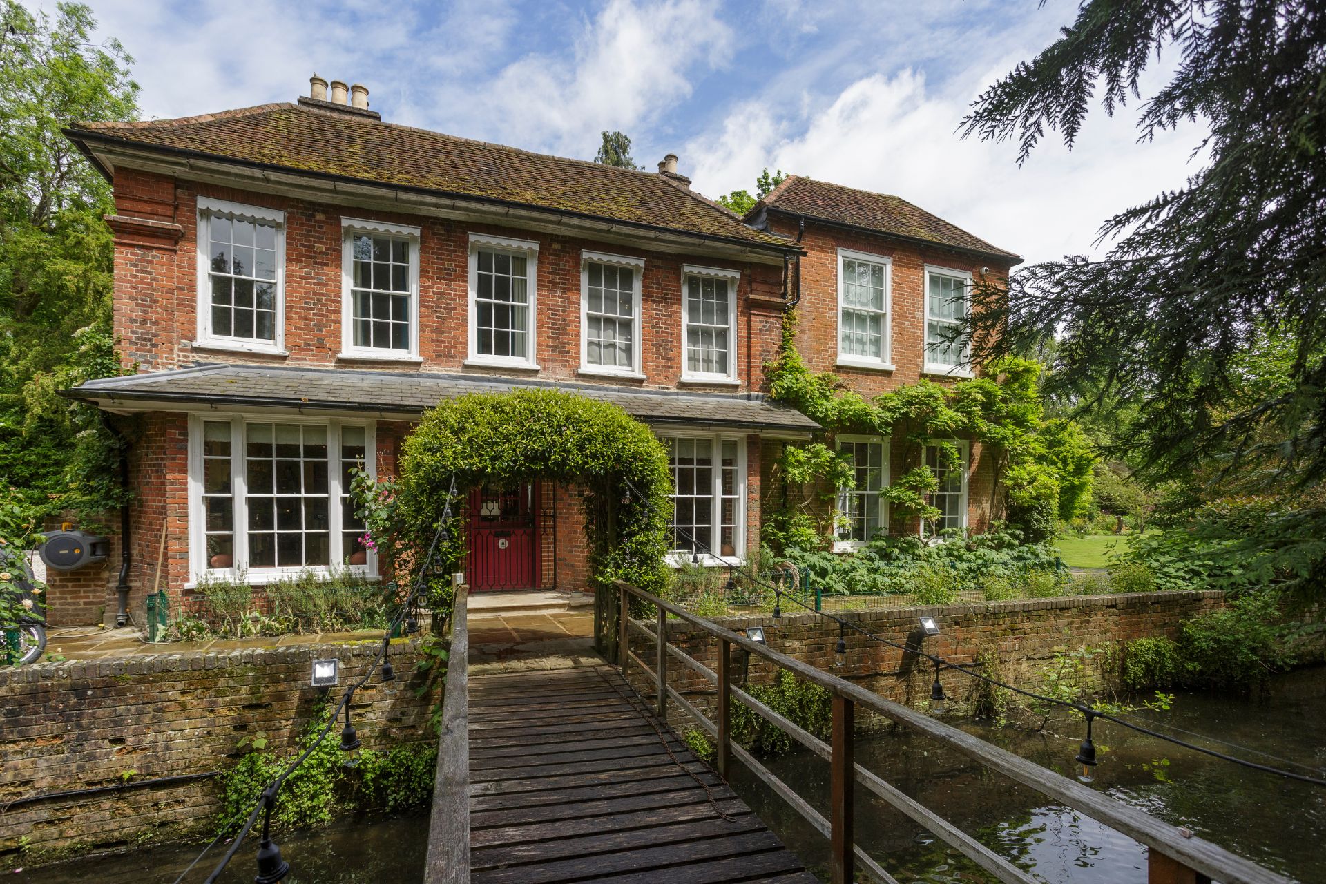 Resar of red brick country home with wooden bridge and mill stream