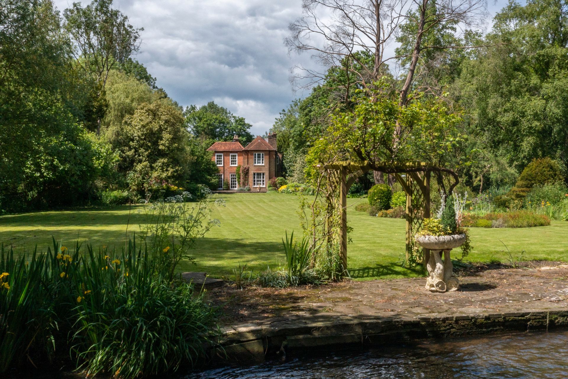 Red brick country home with lawn and stream in the foreground