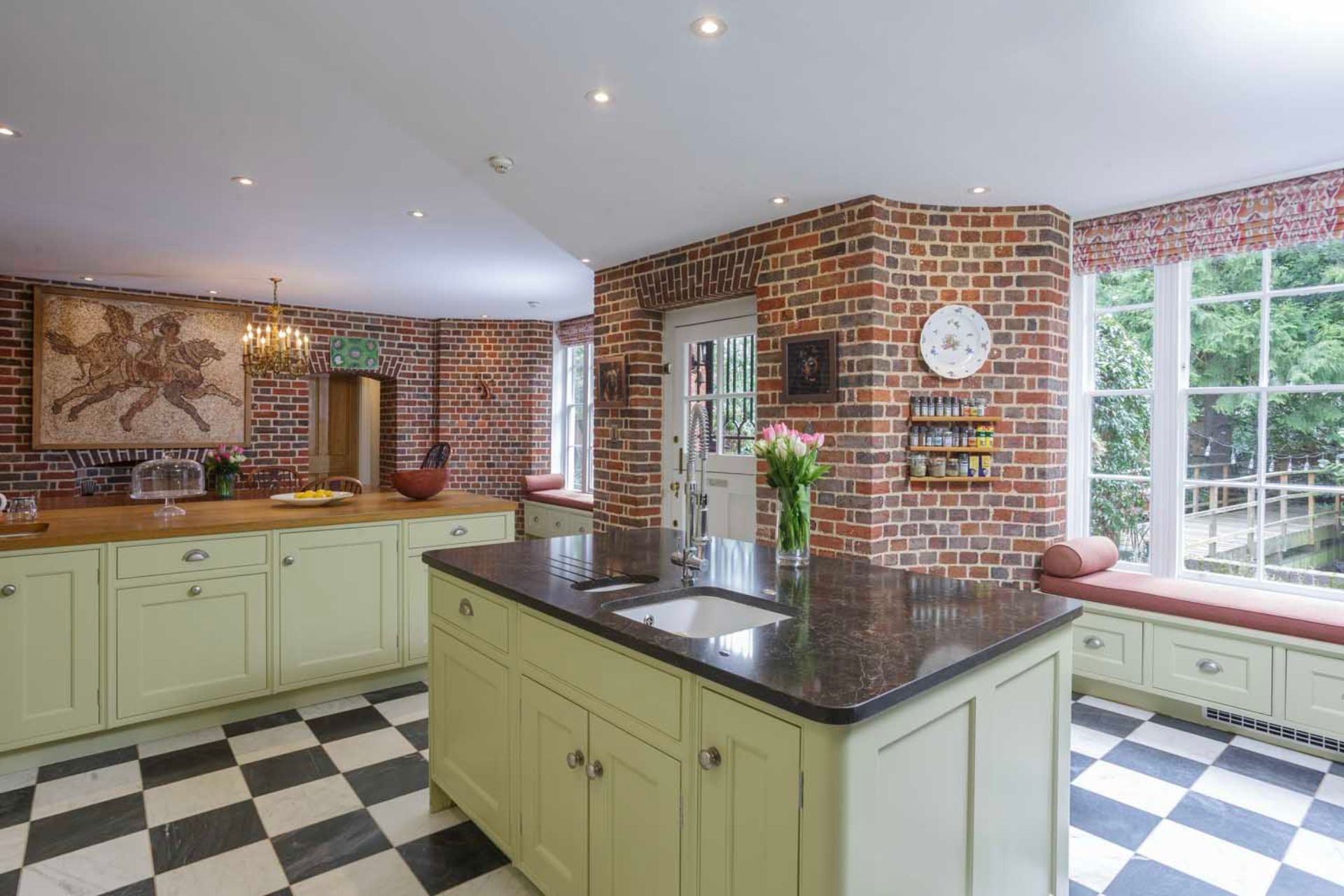 Country kitchen with checkerboard tile flooring, sage green cabinets, and black worktops