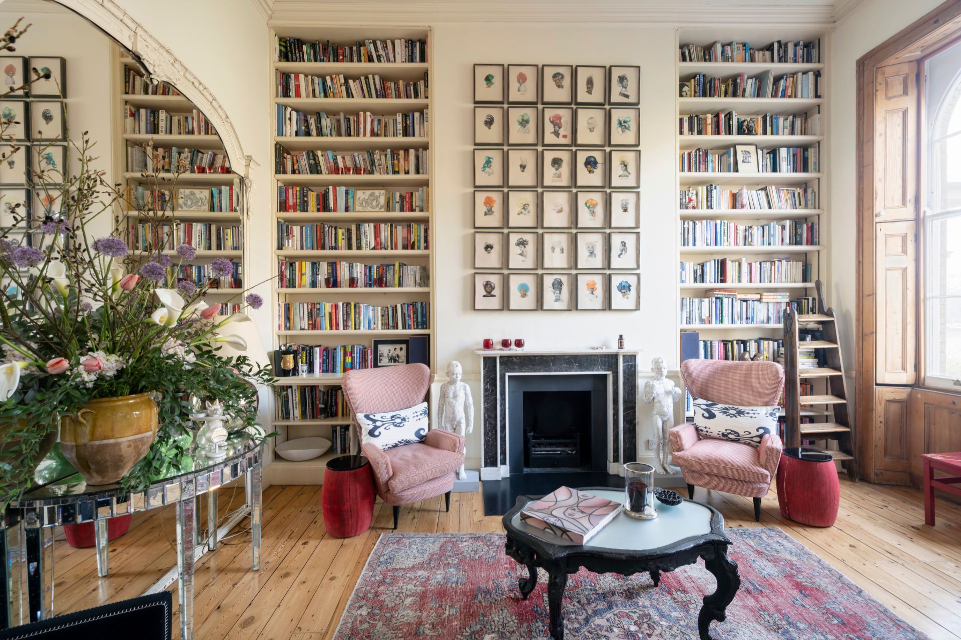 Drawing room with wood floors, built-in bookshelves, dusty pink archairs and a period fireplace