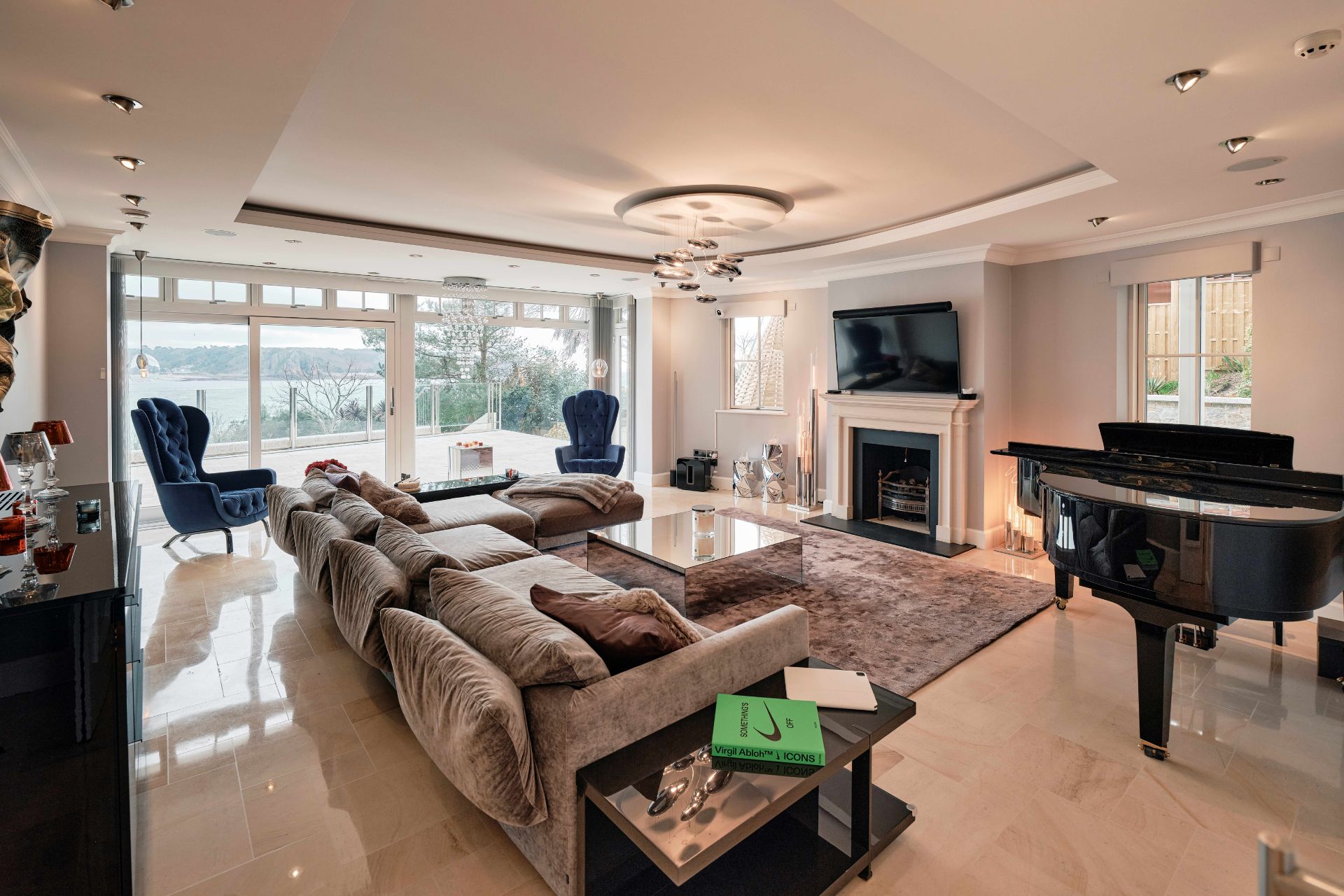 Living room with grand piano, marble fireplace and taupe sofas