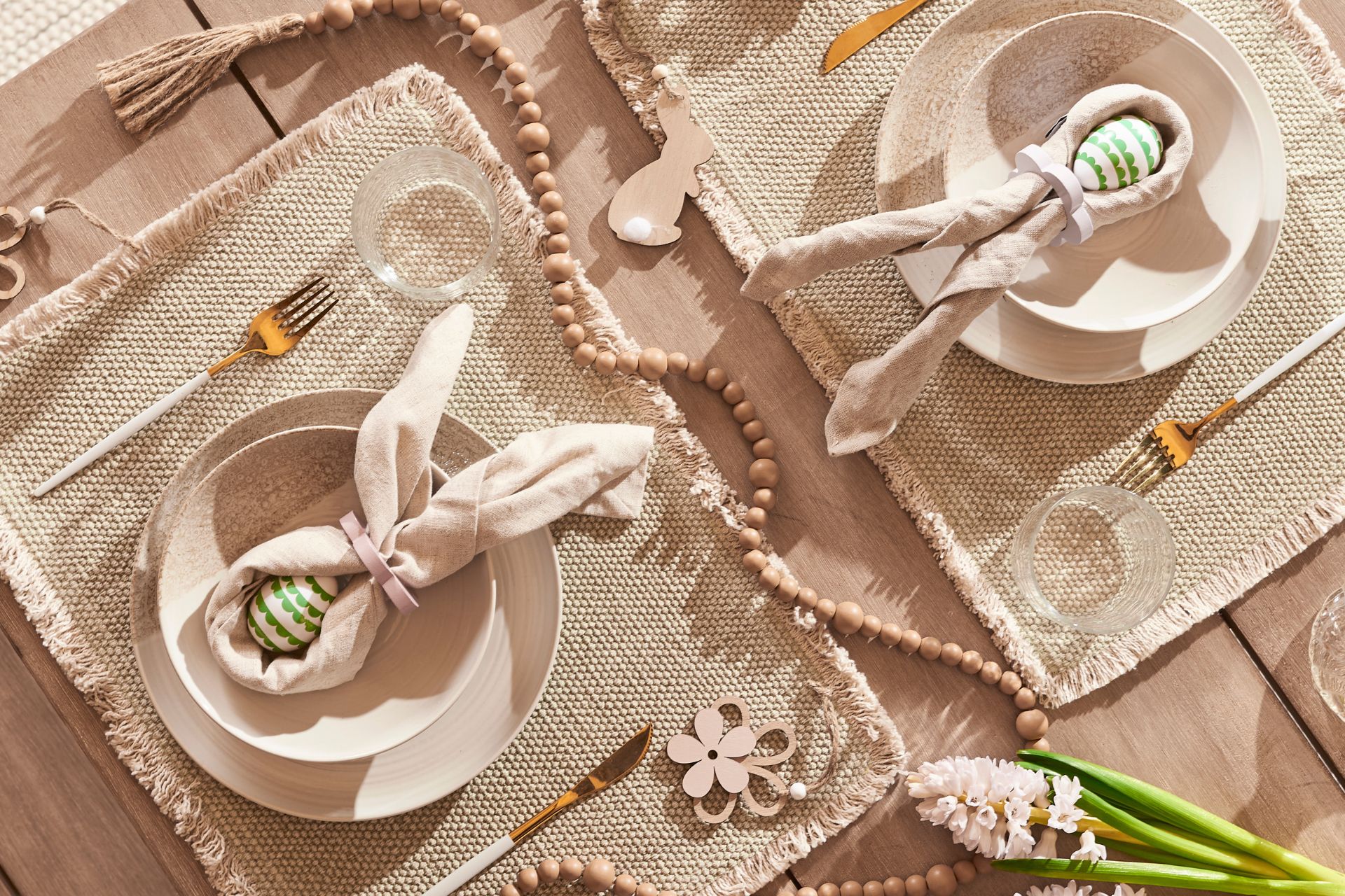 Easter tablescape with beige linen placeats and pale pink napkins tied to look like bunny ears