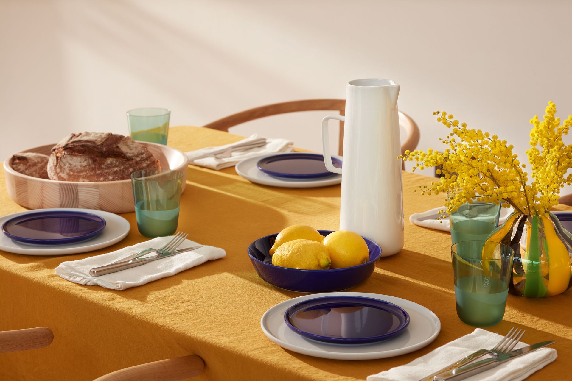 Deep yellow tablecloth with blue side plates, green glassware and yellow flowers