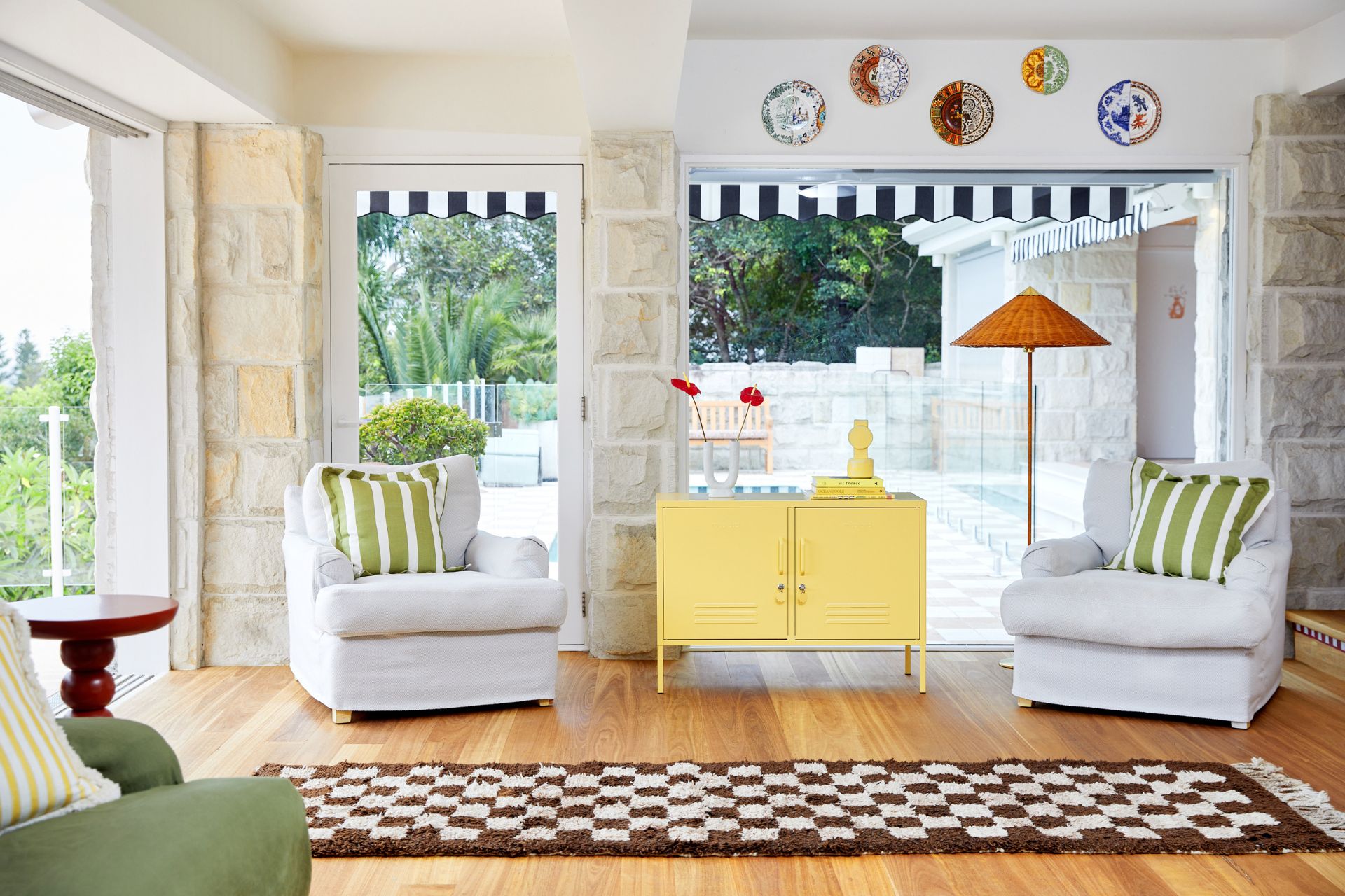 Villa living room with white armchairs, green and white striped cushions, a brown checkerboard runner and a butter yellow sideboard