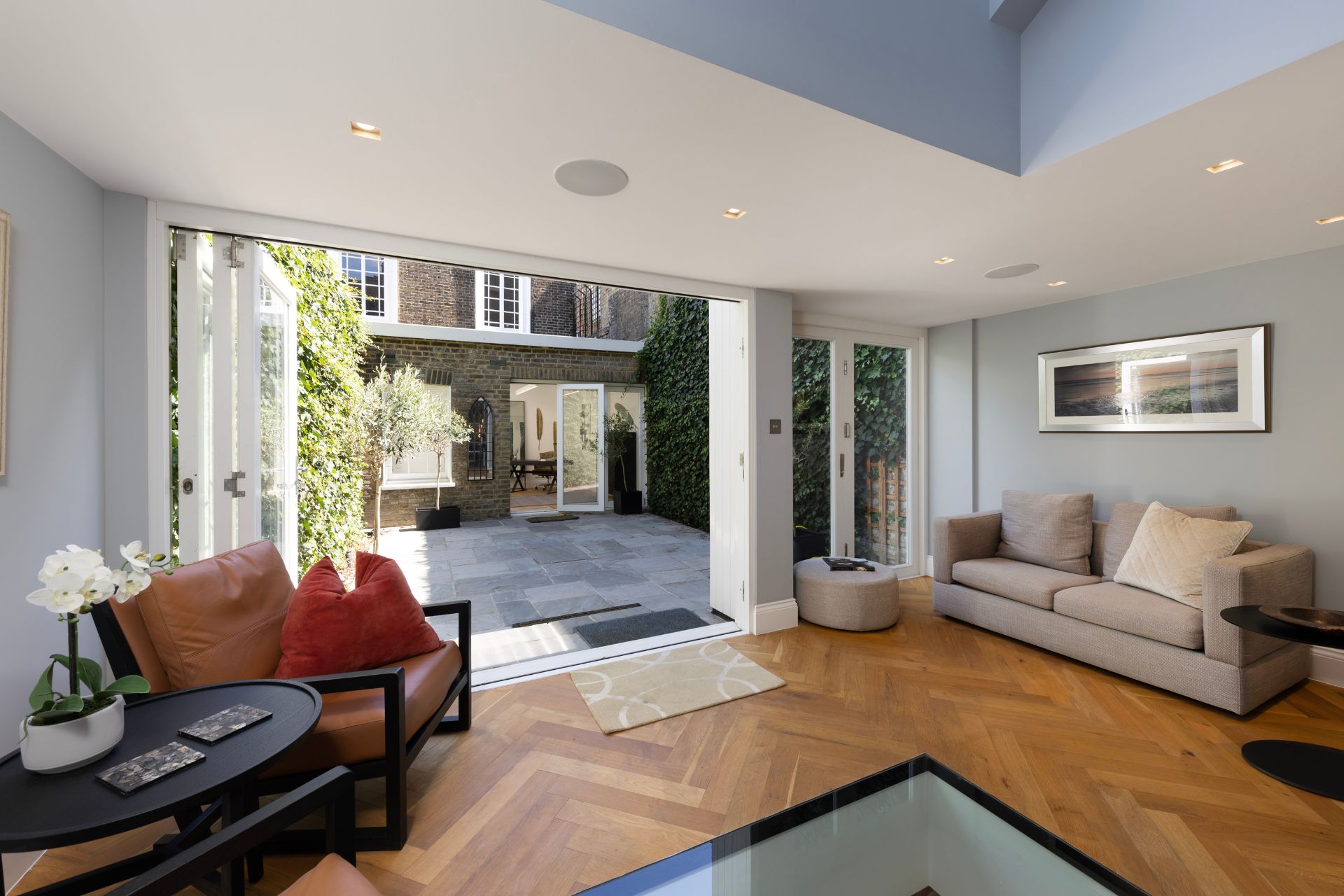 Lounge area with taupe sofas, parquet floors, and bi-fold doors opening onto a patio garden