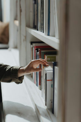 A hand reaching for books on a shelf