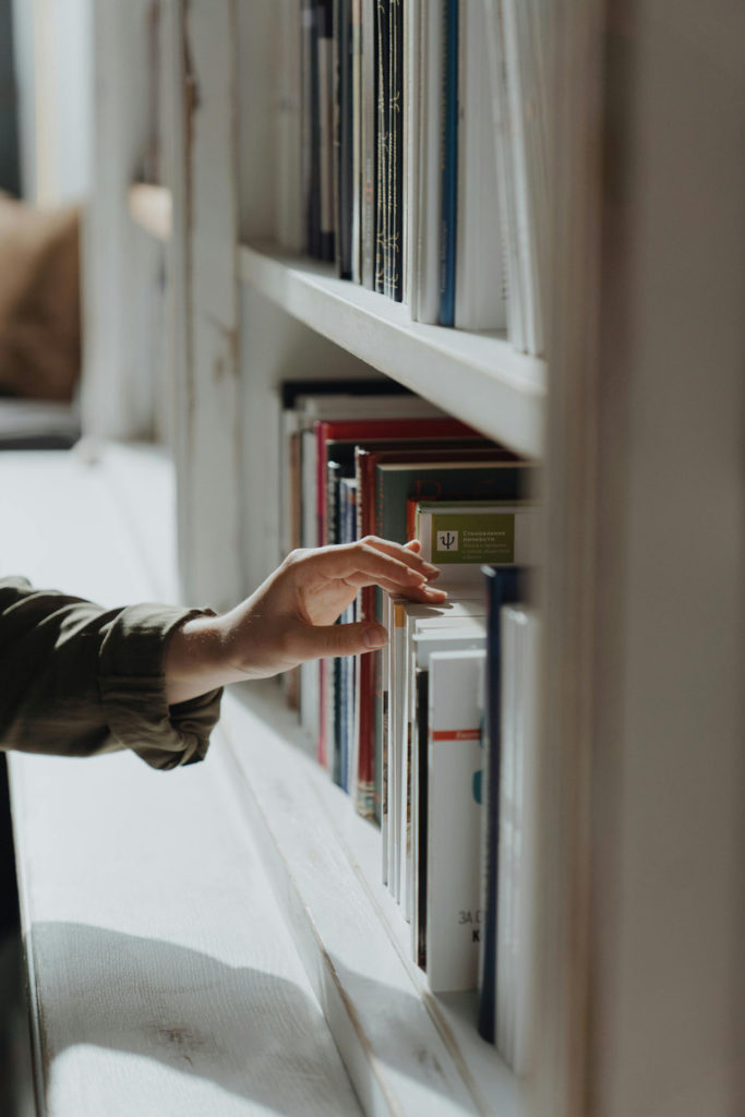A hand reaching for books on a shelf