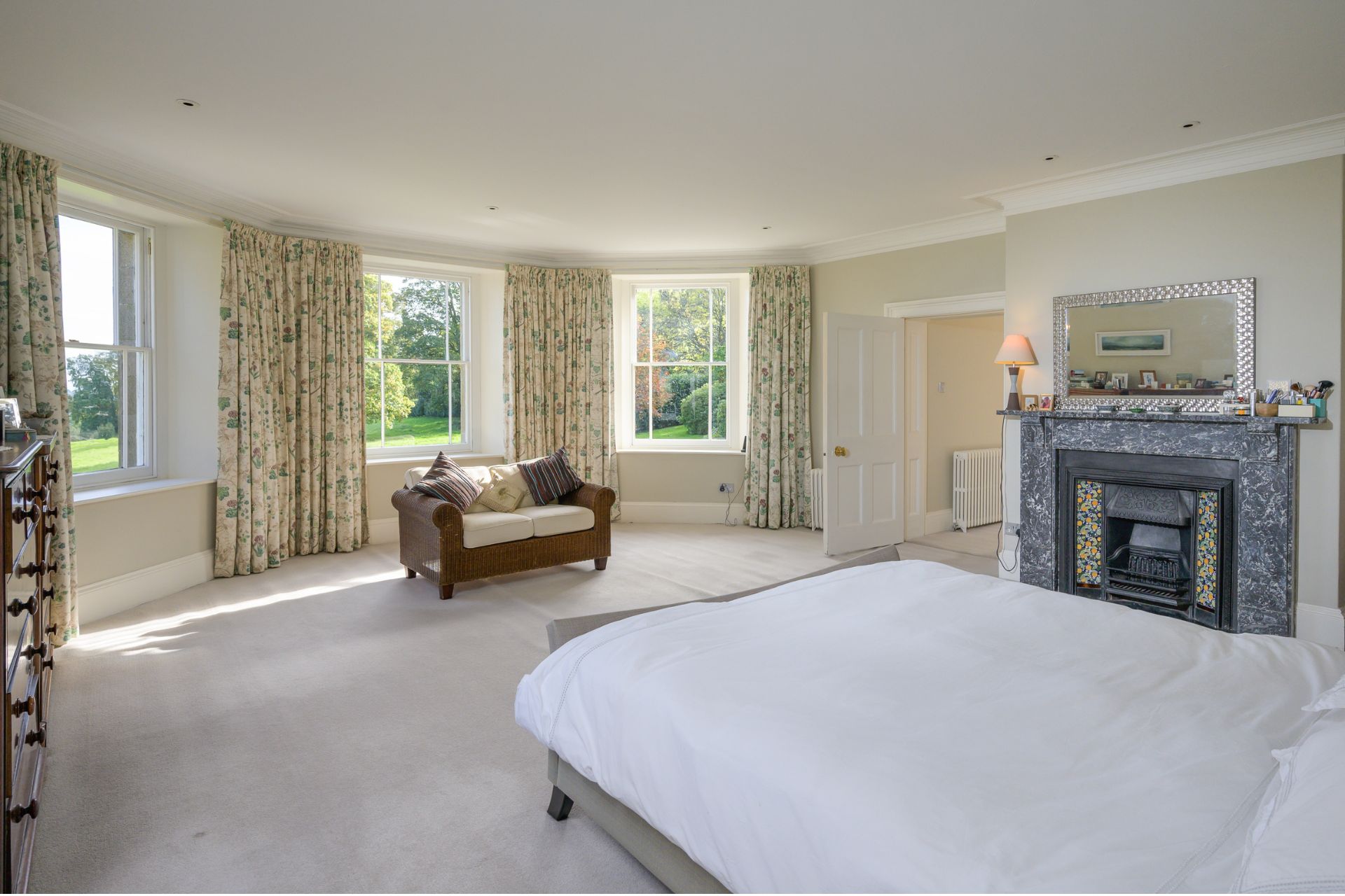 Large bedroom with white bedding and three bay windows with white and green floral curtains