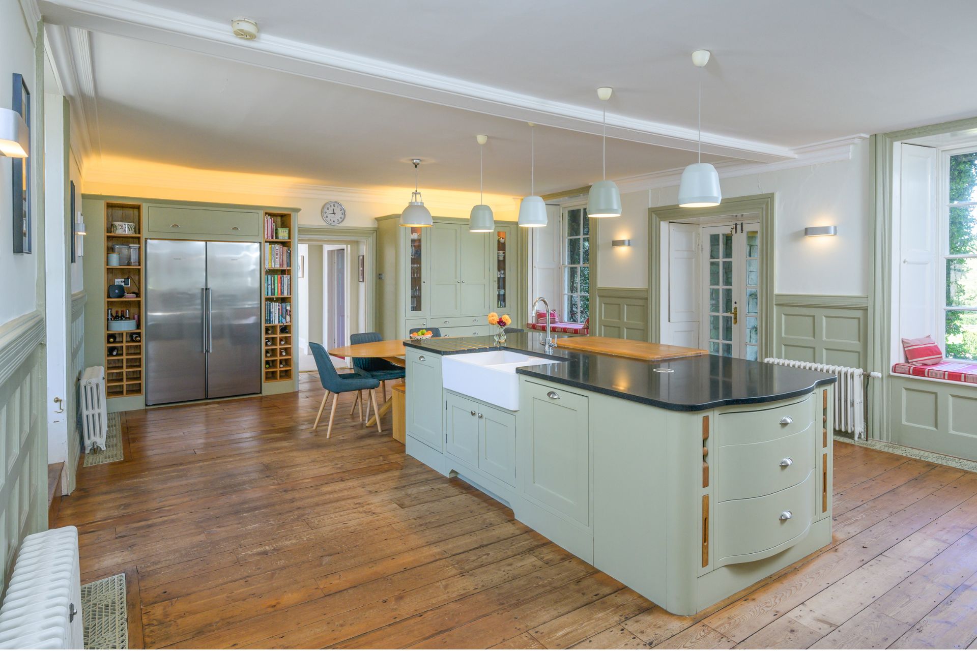 Kitchen with wooden floorboards, sage green cabinets, black granite worktops and an AGA
