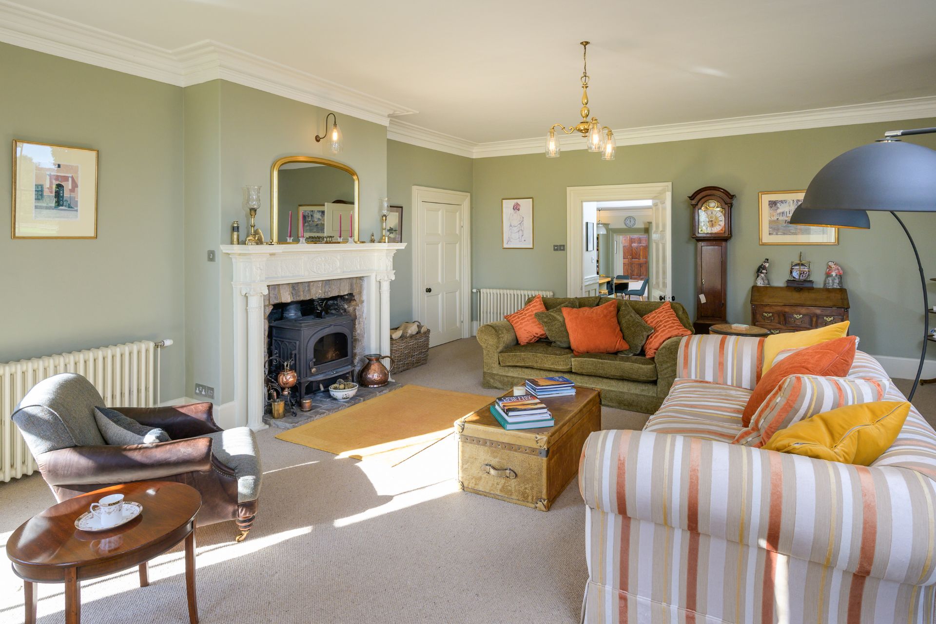Pale green living room with orange and white striped sofas, orange cushions, and a white fireplace