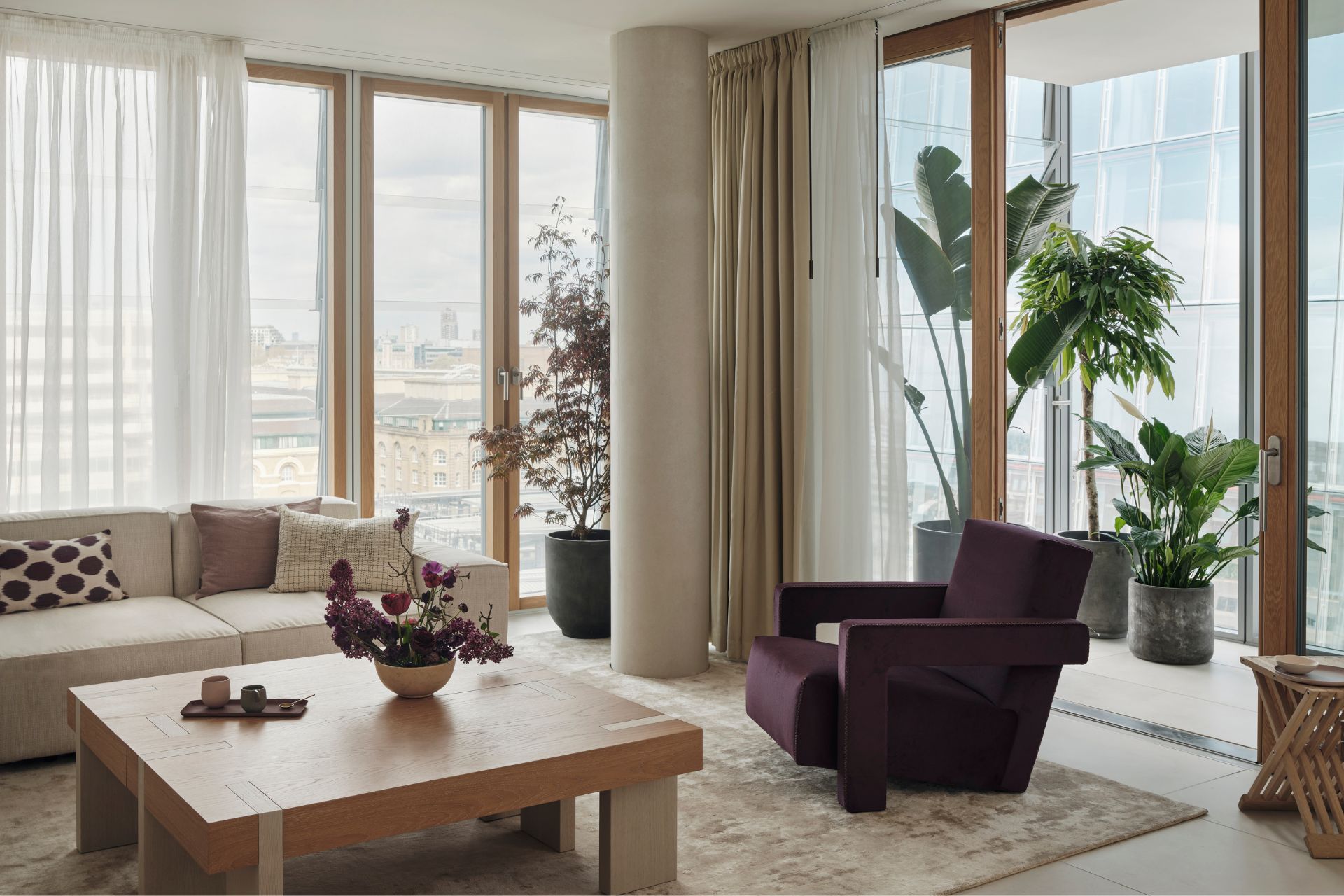 Modern living room with floor-to-ceiling windows, a wooden table and a deep purple armchair