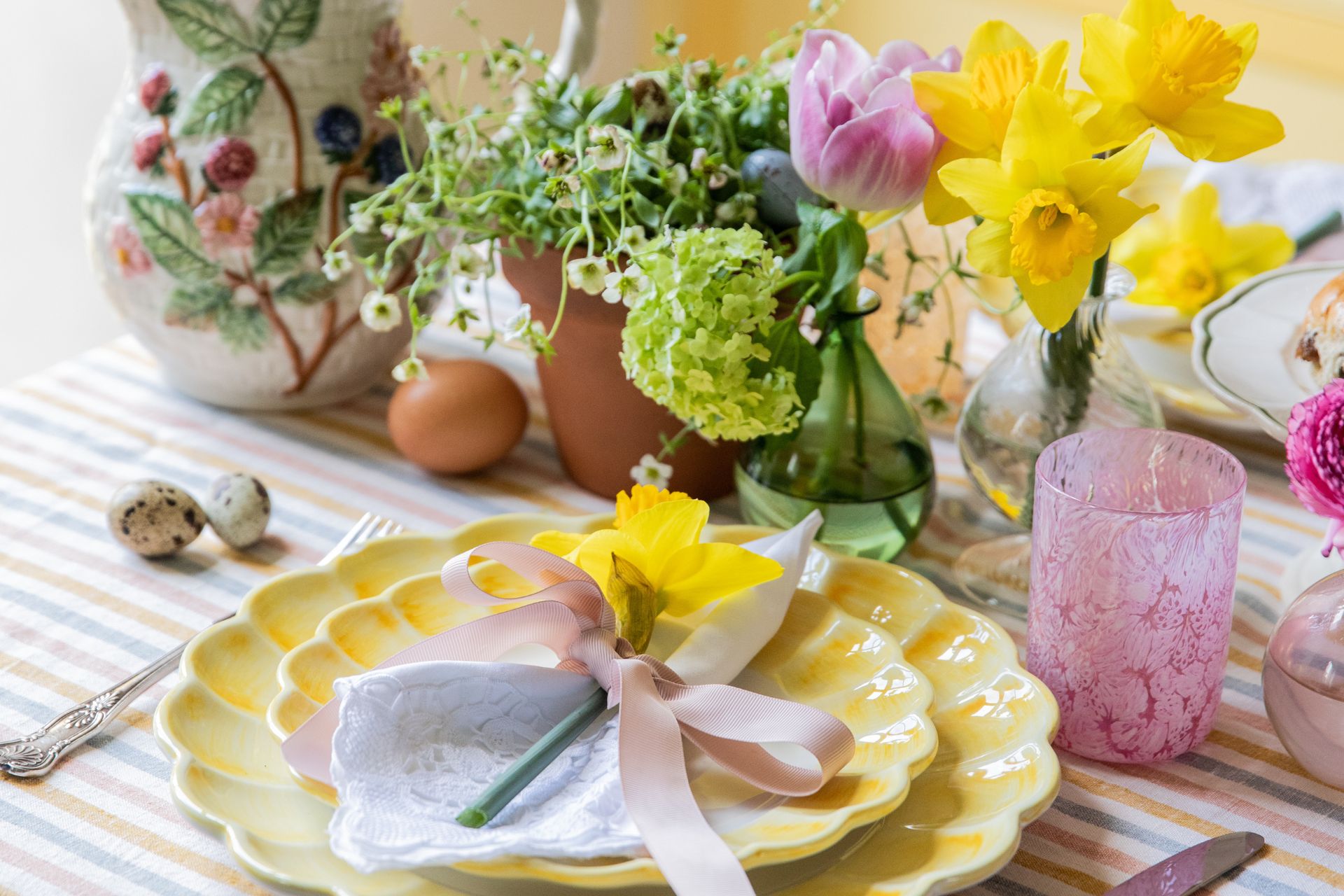 Pastel table with butter yellow plates, pink glassware, a floral jug and vases of fresh flowers