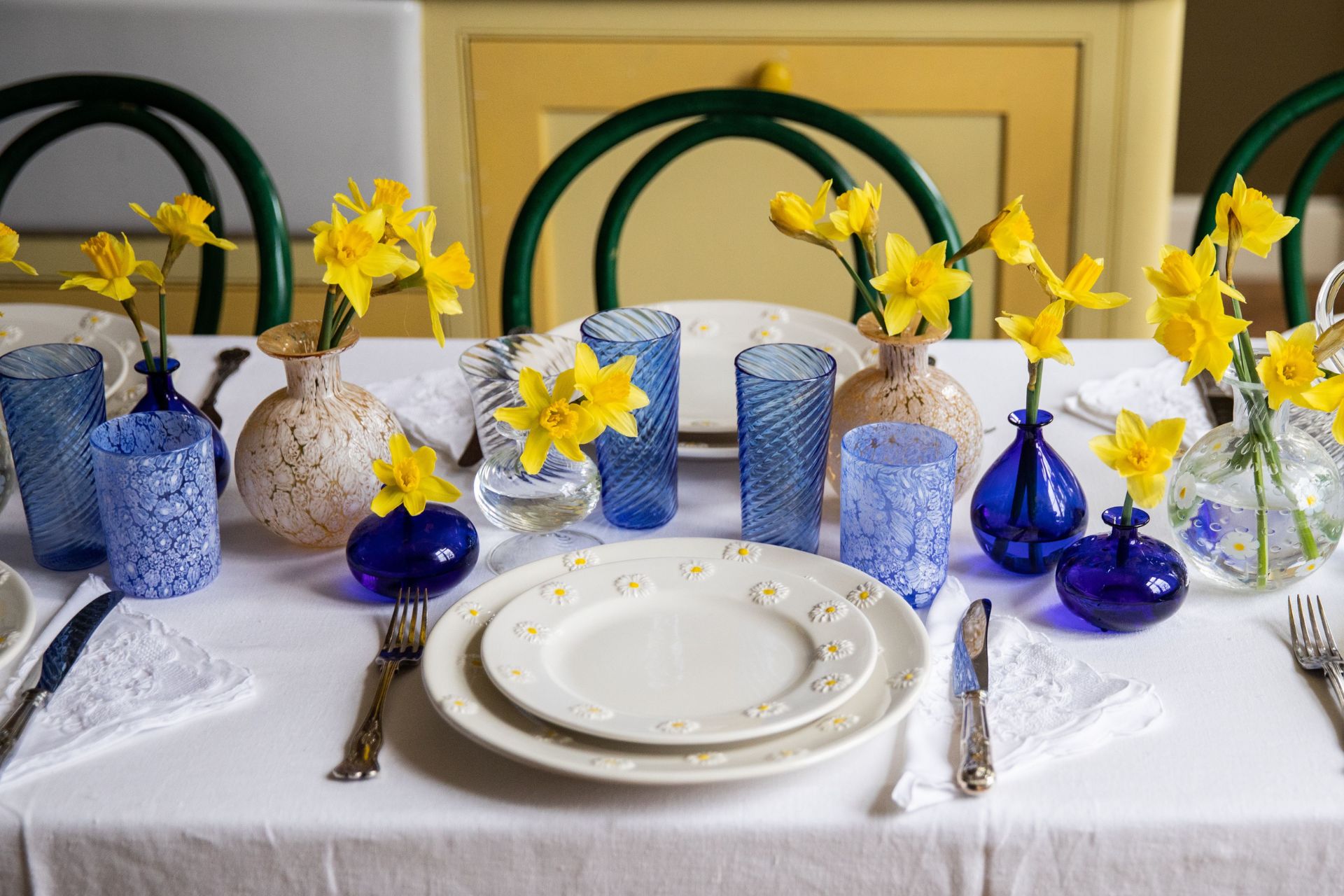 White table with daisy plates, blue glassware, and blue vases full of daffodils