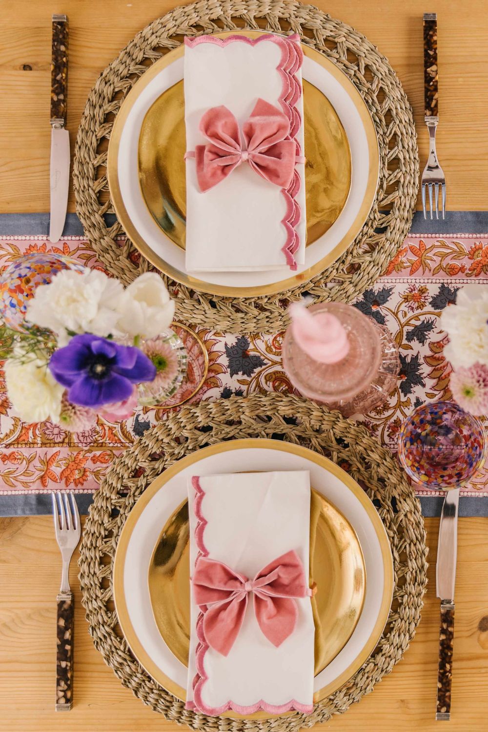 Spring table with pink floral tablecloth, pink scalloped napkins and vases of white and purple flowers