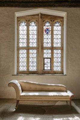 Antique chaise loungue below stained glass windows and white plaster walls