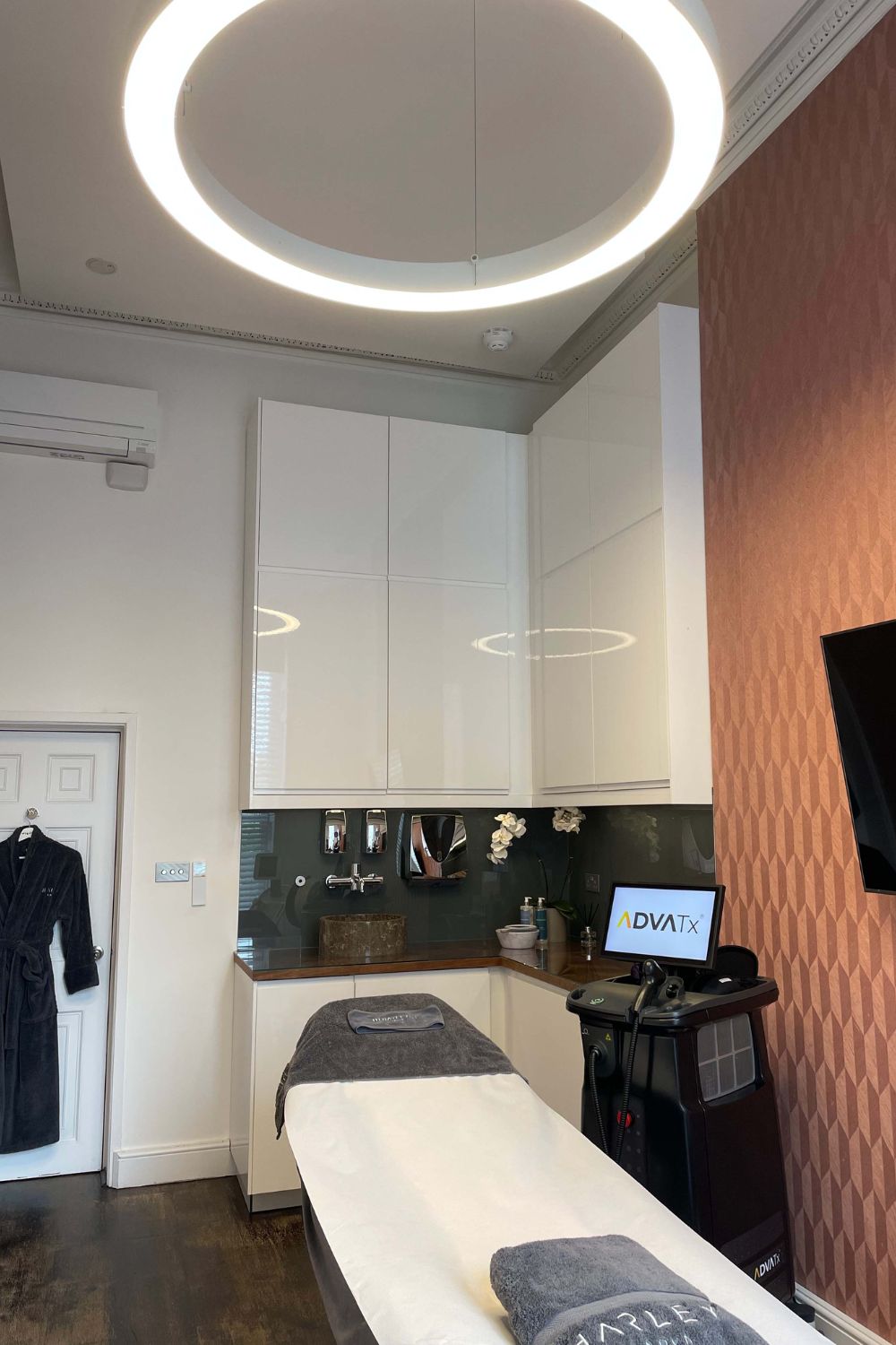 Harley Street treatmnt room with bed, white cabinets, and circular light pendant