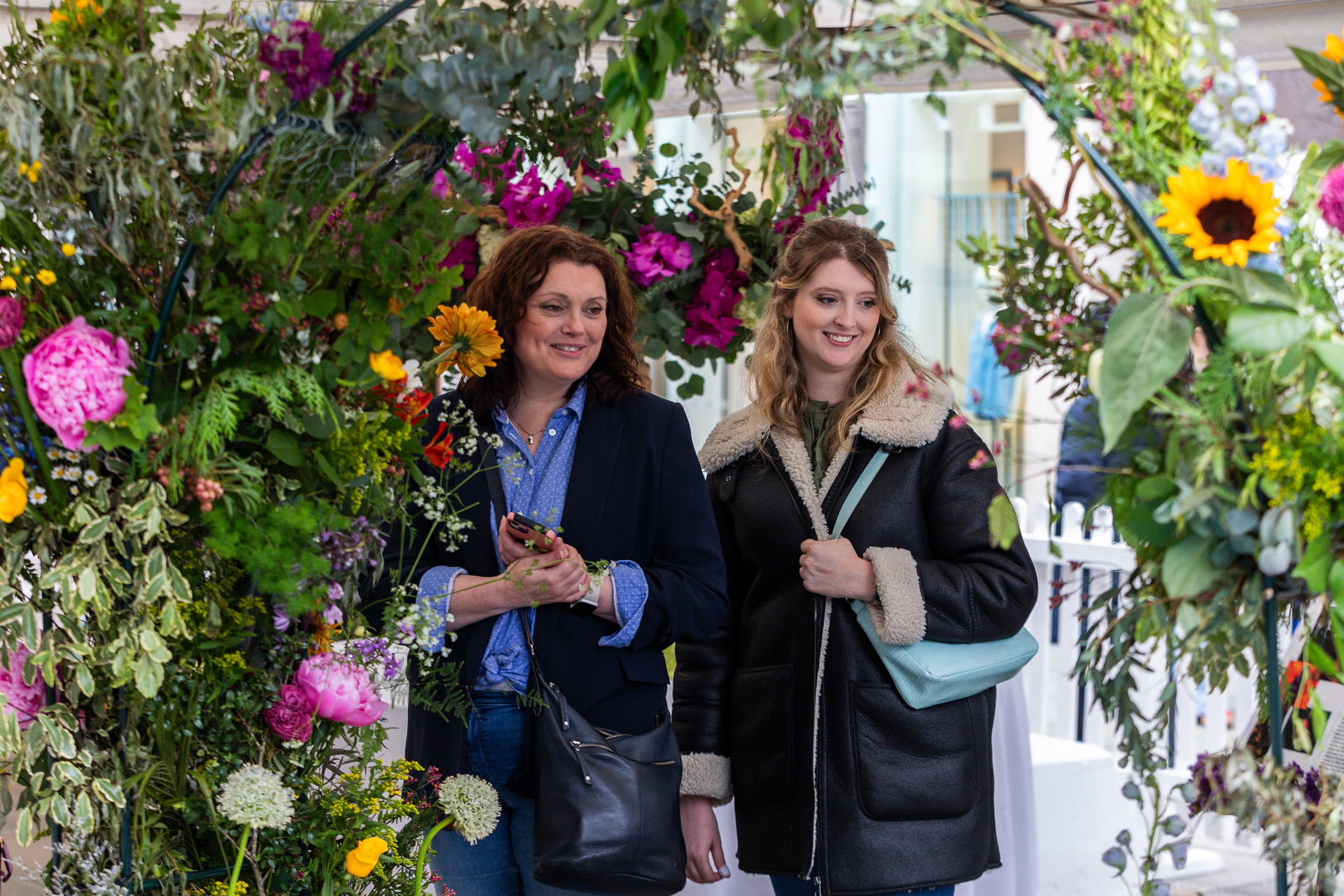 Two women walking through a floral arch