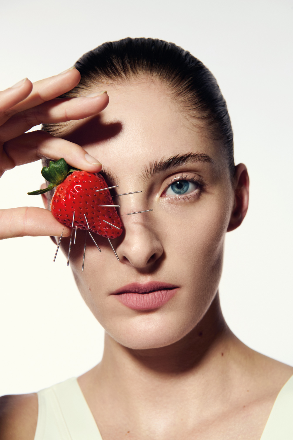 Woman holding punctured strawberry in front of face | aesthetic treatments 2025