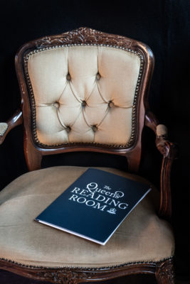 A chair with a book reading Queen’s Reading Room