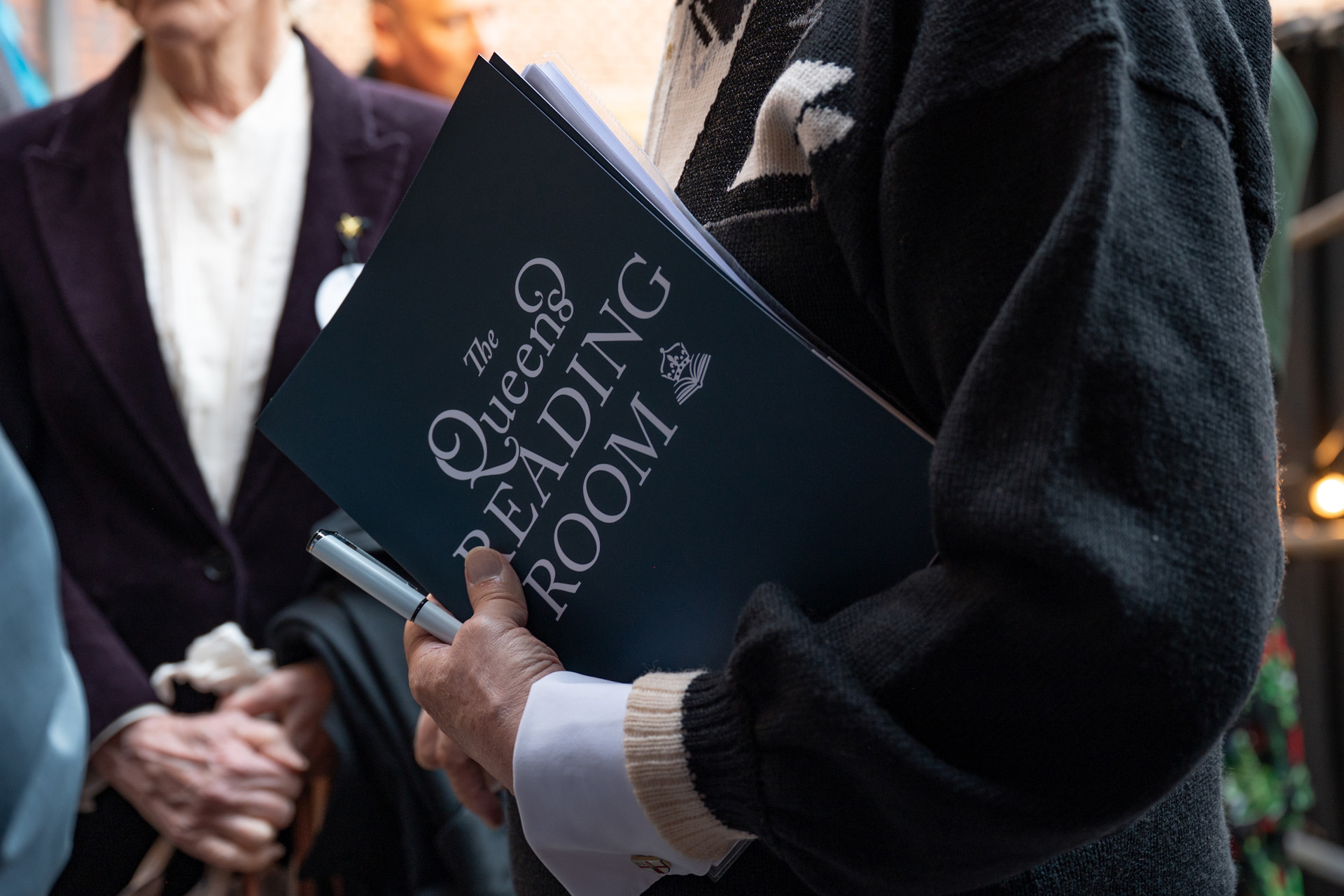A man holding a book reading Queen’s Reading Room