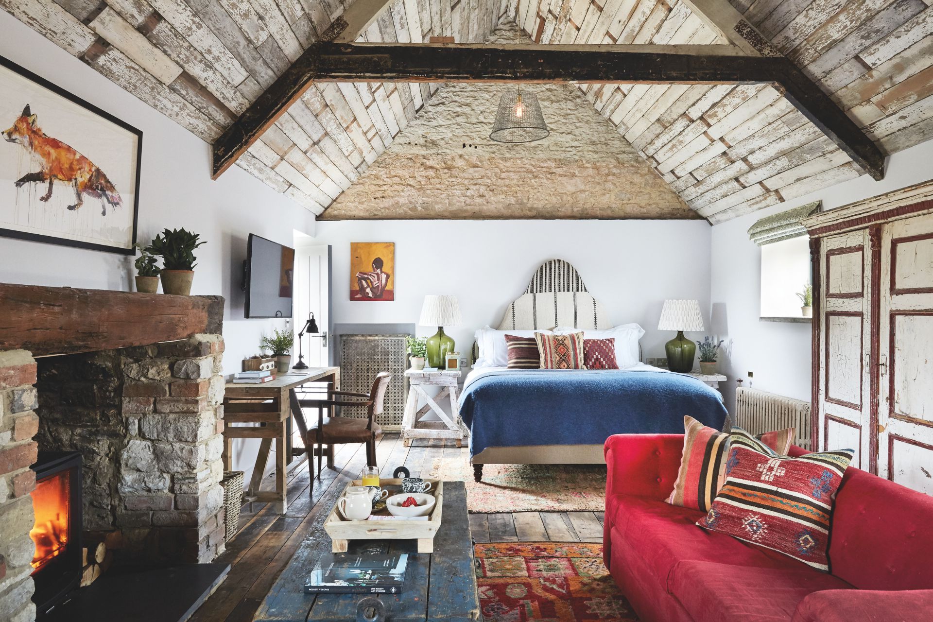 Hotel room with vaulted ceiling, blue bedspread, red sofa and wood floors