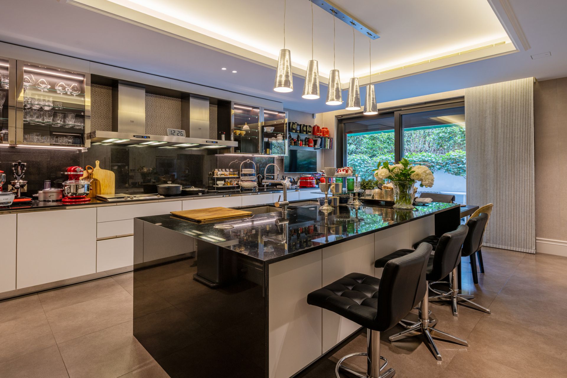 Kitchen with white cabinets, black marble worktops, and black leather bar stools