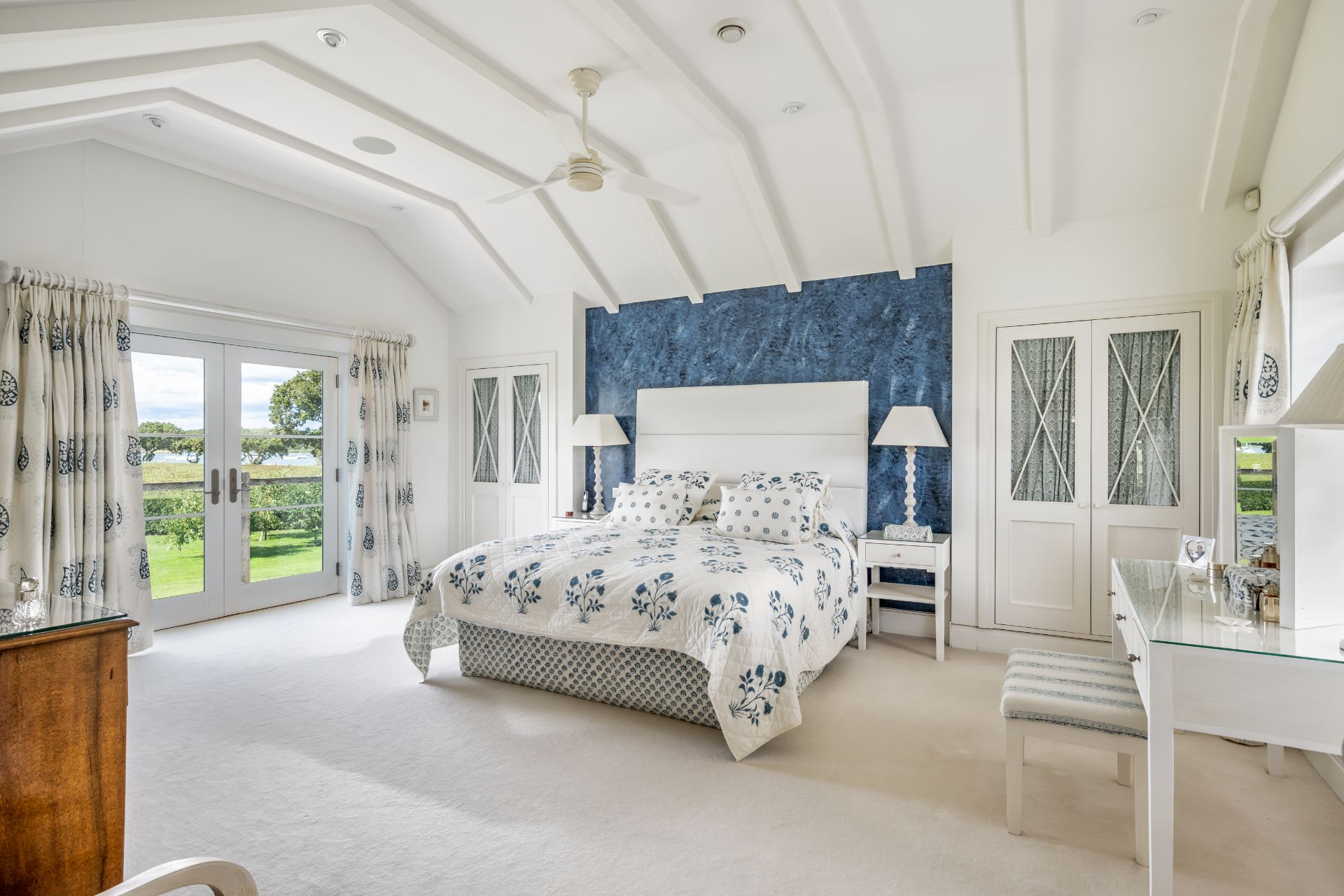 Bedroom with vaulted ceilings, blue headboard and doors leading onto a balcony