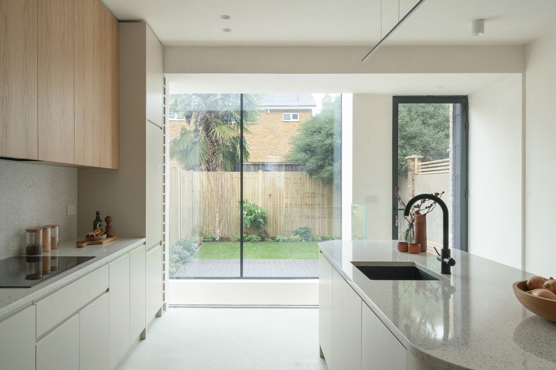 Japandi-style kitchen with pale wooden cabinets, white stonew worktops and floor-to-ceiling sliding doors.