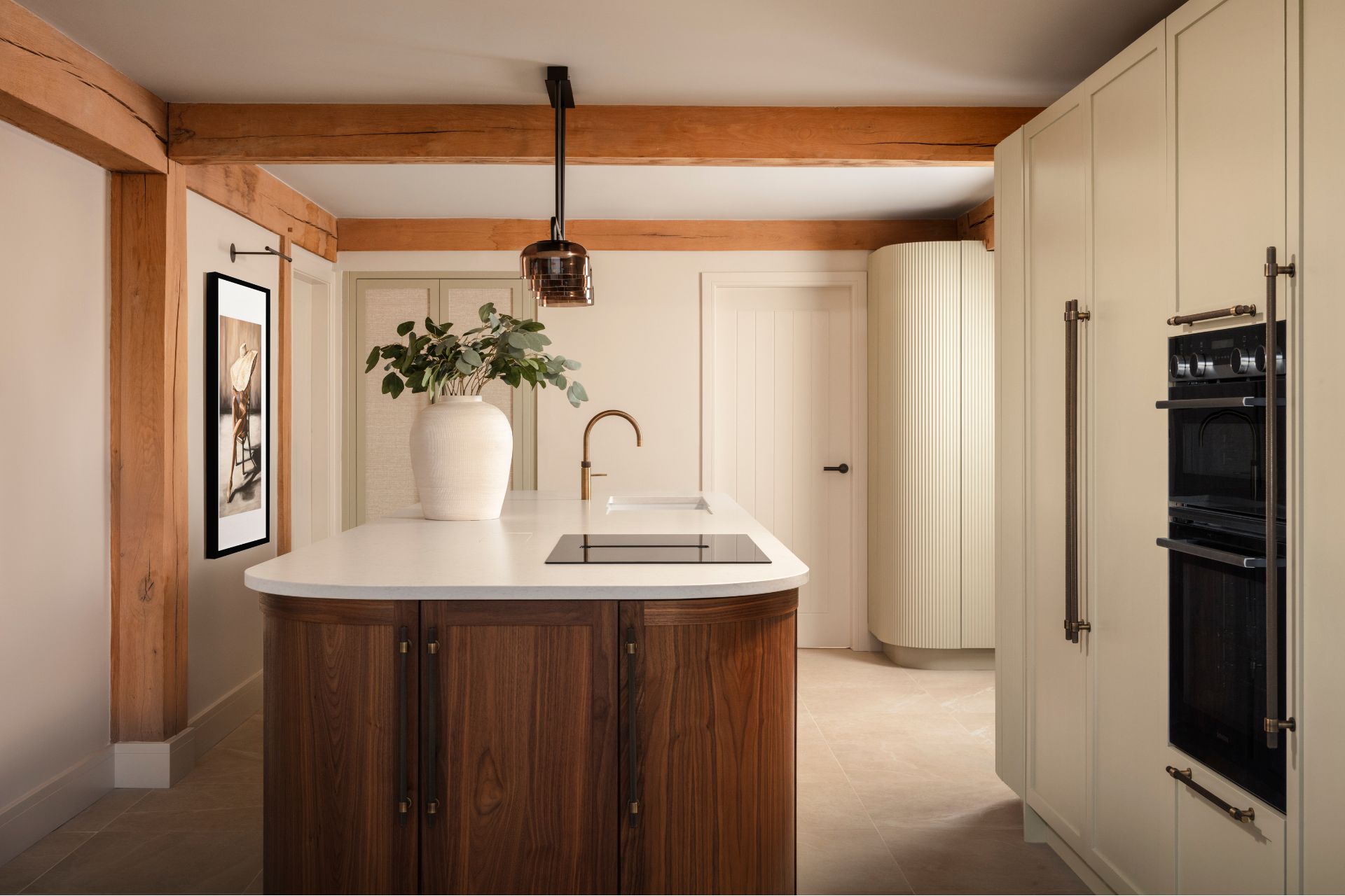 Kitchen with dark wooden curved island, white worktops, and cream fluted cabinets