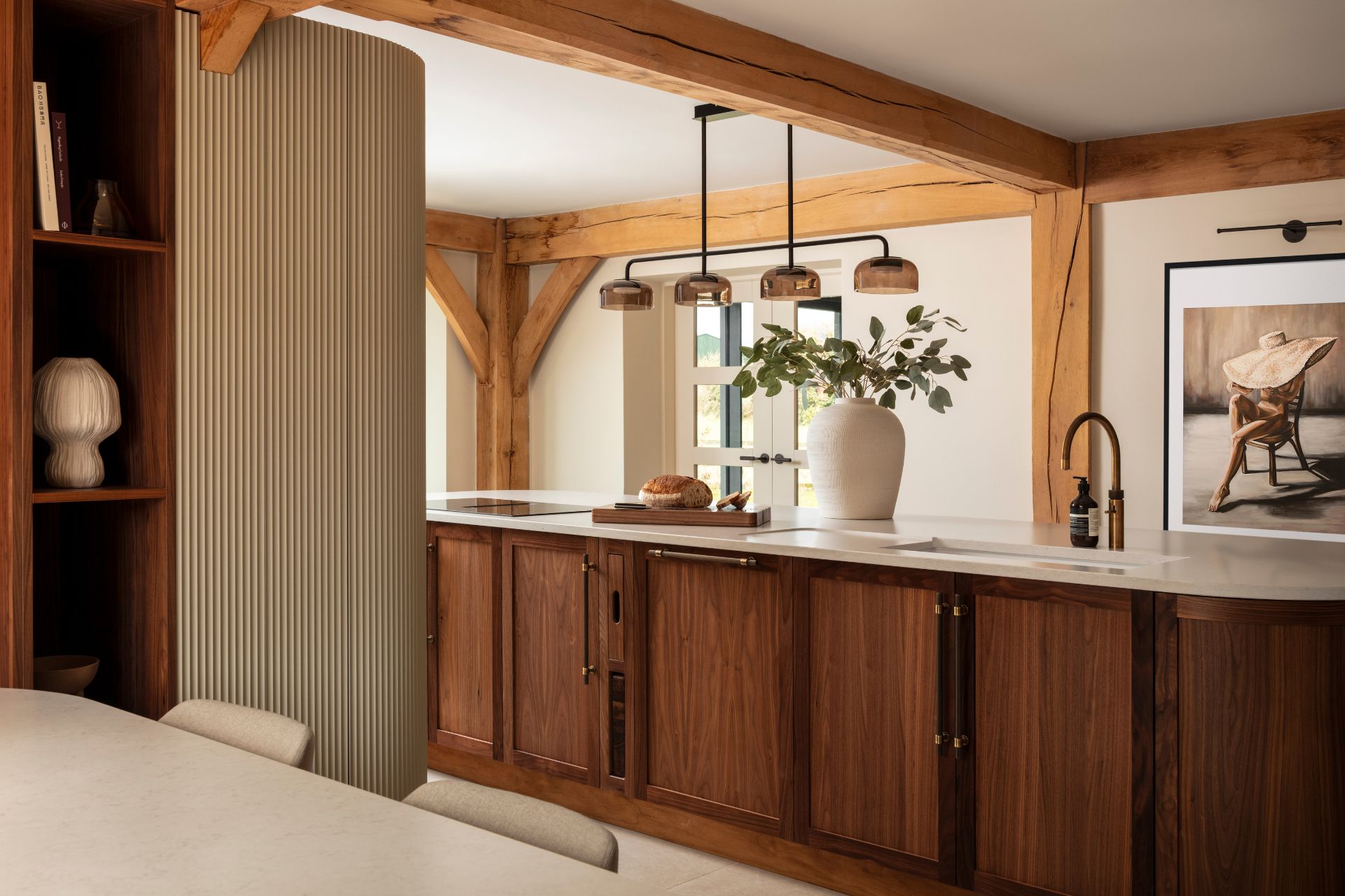 Kitchen with dark wooden island, white worktops, and curved fluted tall cabinets